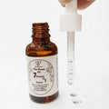 Amber glass bottle of Beauty with Care 7 Serums in 1 with open dropper and serum drops