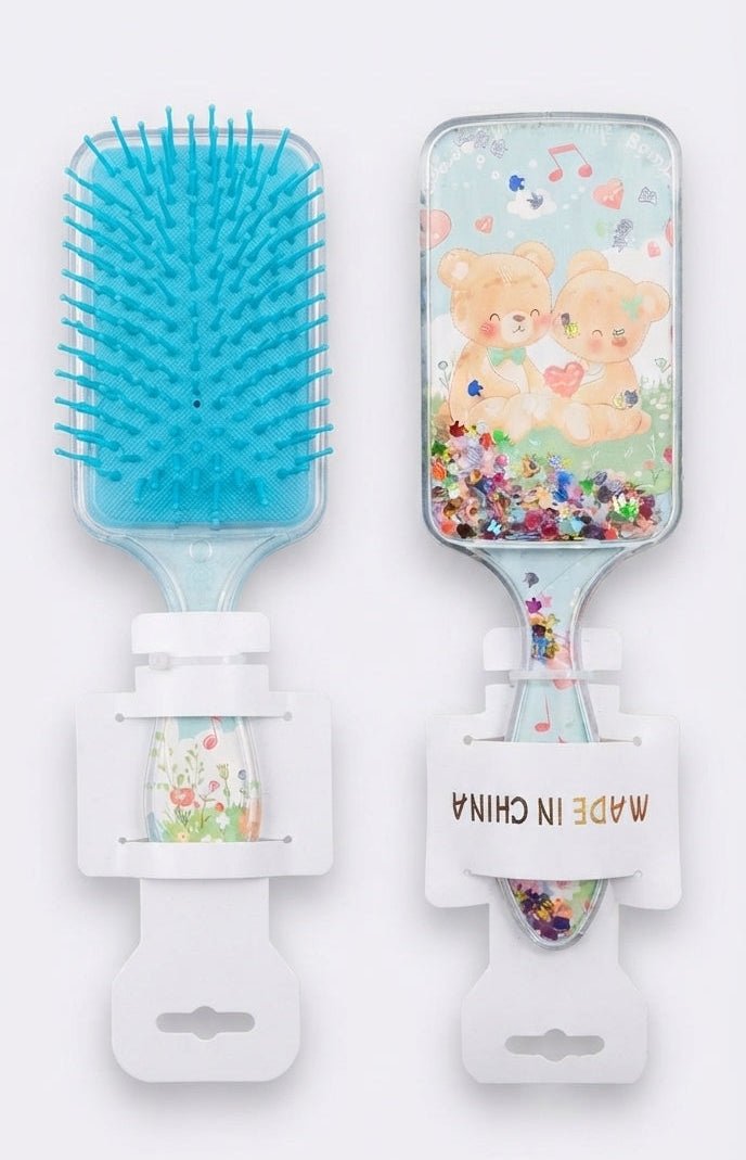 Two small handheld hairbrushes shown side by side on a plain light background. One brush has bright blue bristles, and the other features a clear container with floating multicolor glitter and two cute kissing bear illustrations.