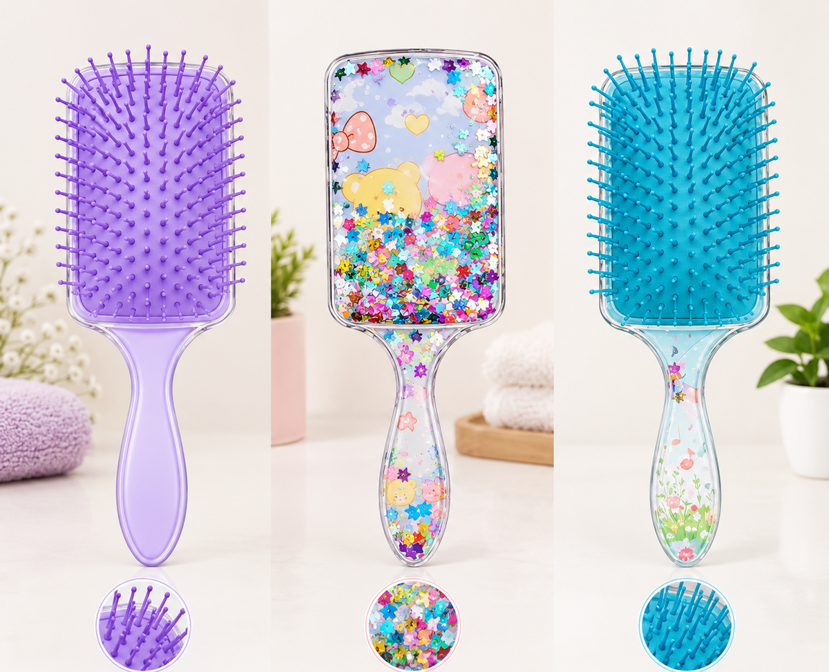 Three hairbrushes shown side by side on a light studio background, each with a different color and glitter design: a lavender purple soft brush, a multicolor glitter paddle brush, and a bright blue comfortable grip brush.