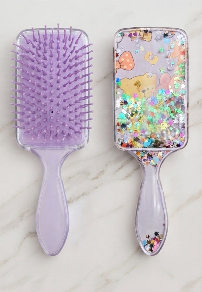 Two lavender hairbrushes shown side-by-side on a light marble surface. The left brush features solid lavender bristles and handle, while the right brush contains clear liquid, multicolor glitter, and cute purple bear illustrations.