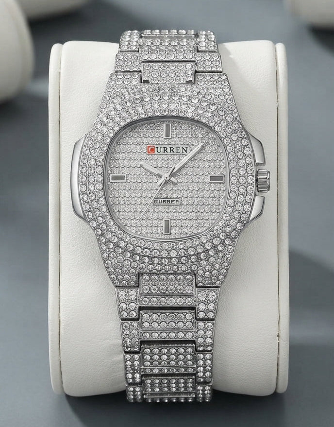 A heavily embellished silver-tone wristwatch covered in sparkling rhinestones, displayed on a dark marble surface with jewelry props around it.