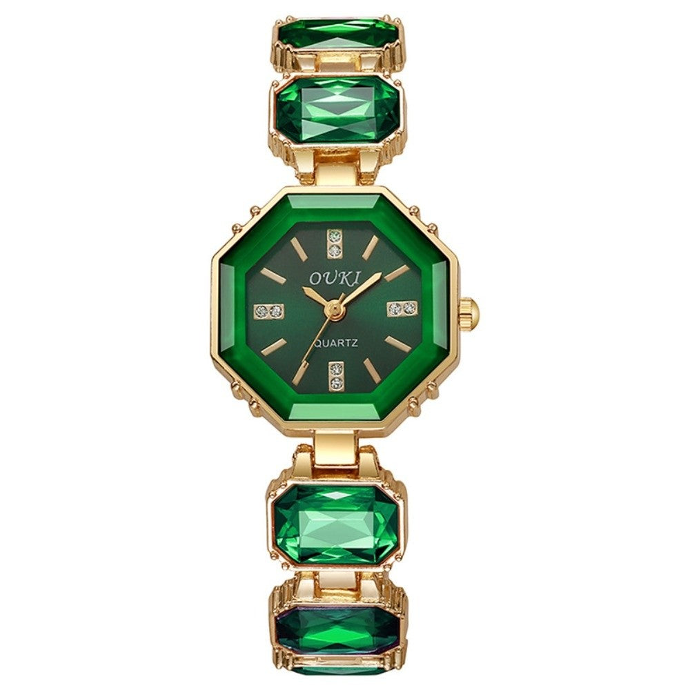 Green and gold watch with emerald-like stones on a white background.
