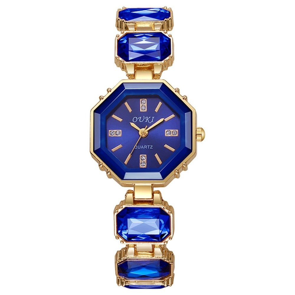 A women's gold-tone octagonal watch with a sapphire blue dial and blue rectangular crystal links on a white background.