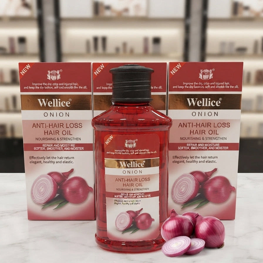 A bottle of Wellice Onion Anti-Hair Loss Hair Oil flanked by two matching product boxes, decorated with fresh red onions on a marble surface.